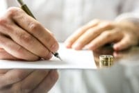 Man signing divorce papers with ring on the table